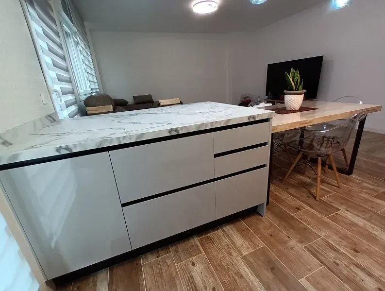 Una moderna isla de cocina con encimera de mármol, armarios de colores claros y una mesa de comedor contigua sobre un suelo de madera.