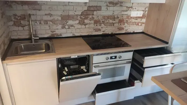 Una cocina moderna con armarios de madera clara, salpicadero con diseño de ladrillo, fregadero de acero inoxidable y lavavajillas y cajones abiertos.