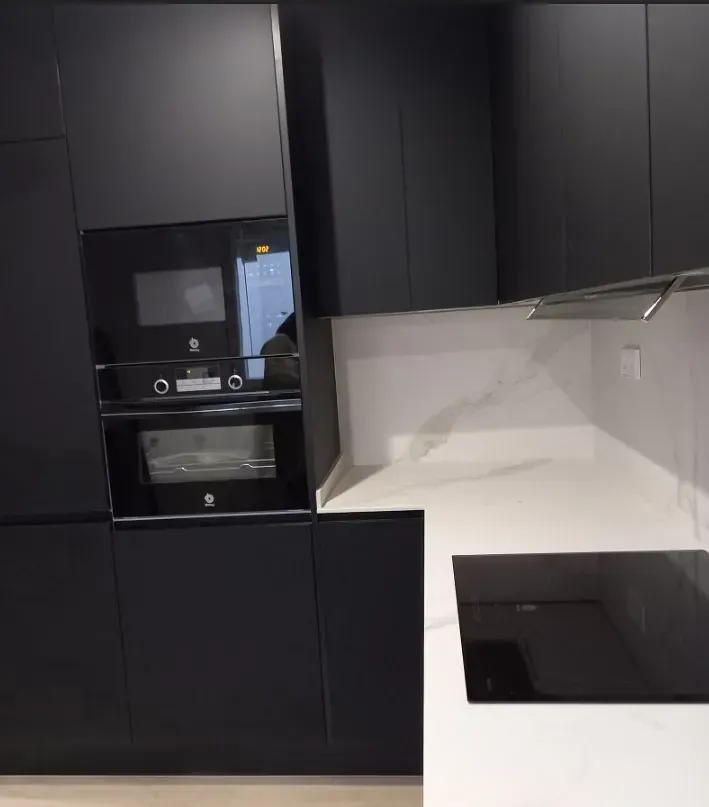 Una cocina moderna con elegantes armarios en negro mate, electrodomésticos integrados y encimeras con diseño de mármol blanco.