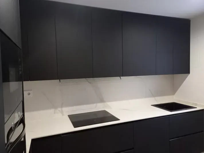 Una cocina moderna con armarios negros mate, salpicadero y encimera con vetas de mármol blanco, placa de inducción y fregadero.