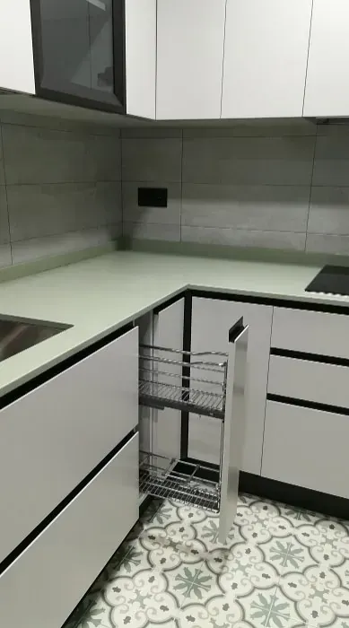 Una encimera de cocina con armarios blancos y un especiero extraíble de alambre abierto, sobre un suelo de baldosas estampadas.