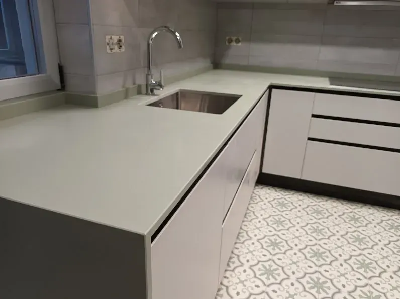 Un rincón de cocina moderno con armarios de color gris claro, una encimera de superficie sólida a juego, un fregadero bajo encimera y suelos de baldosas.
