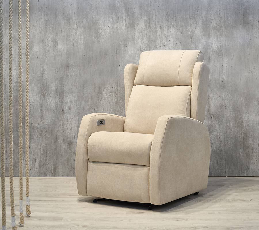 En una habitación con una pared con textura de hormigón y suelo de madera clara, hay un sillón reclinable eléctrico tapizado en color beige.