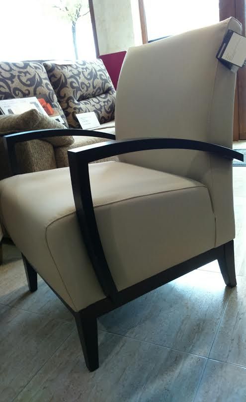 Una silla auxiliar tapizada en color blanco roto con brazos de madera oscura y arqueados, ubicada en un espacio comercial.