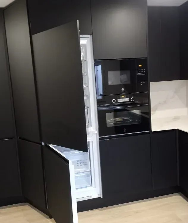 Una cocina moderna con armarios de color negro mate, que incluye un frigorífico integrado con puertas que se abren y un horno empotrado.