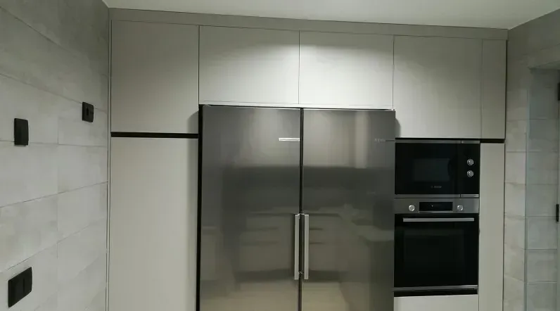 Una pared de cocina moderna con gabinetes gris claro, un refrigerador de acero inoxidable y un horno y microondas empotrados.