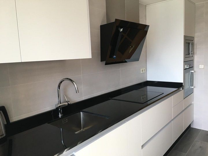 Una cocina moderna con armarios blancos, encimera negra, fregadero de acero inoxidable y campana extractora negra.