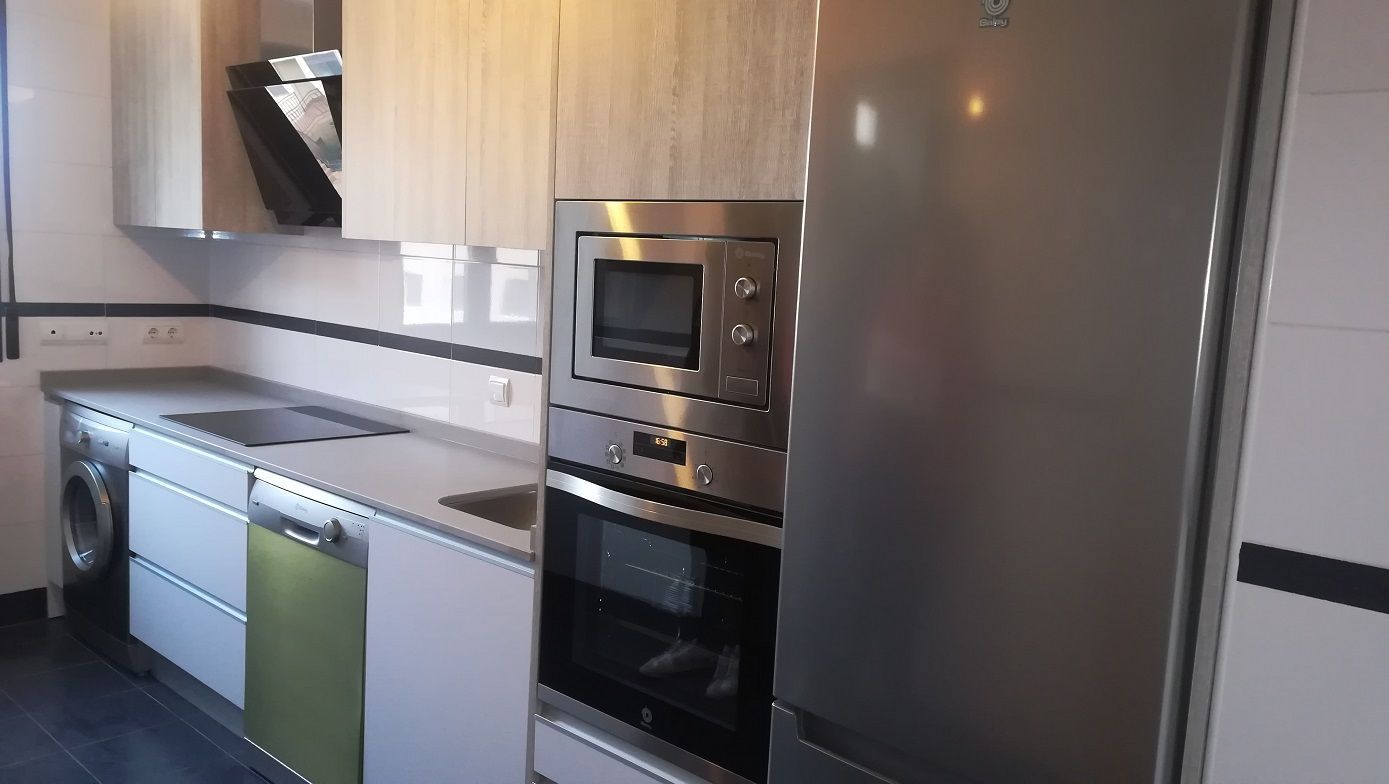 Una cocina moderna con armarios de madera clara, electrodomésticos de acero inoxidable, encimera gris y salpicadero de azulejos.
