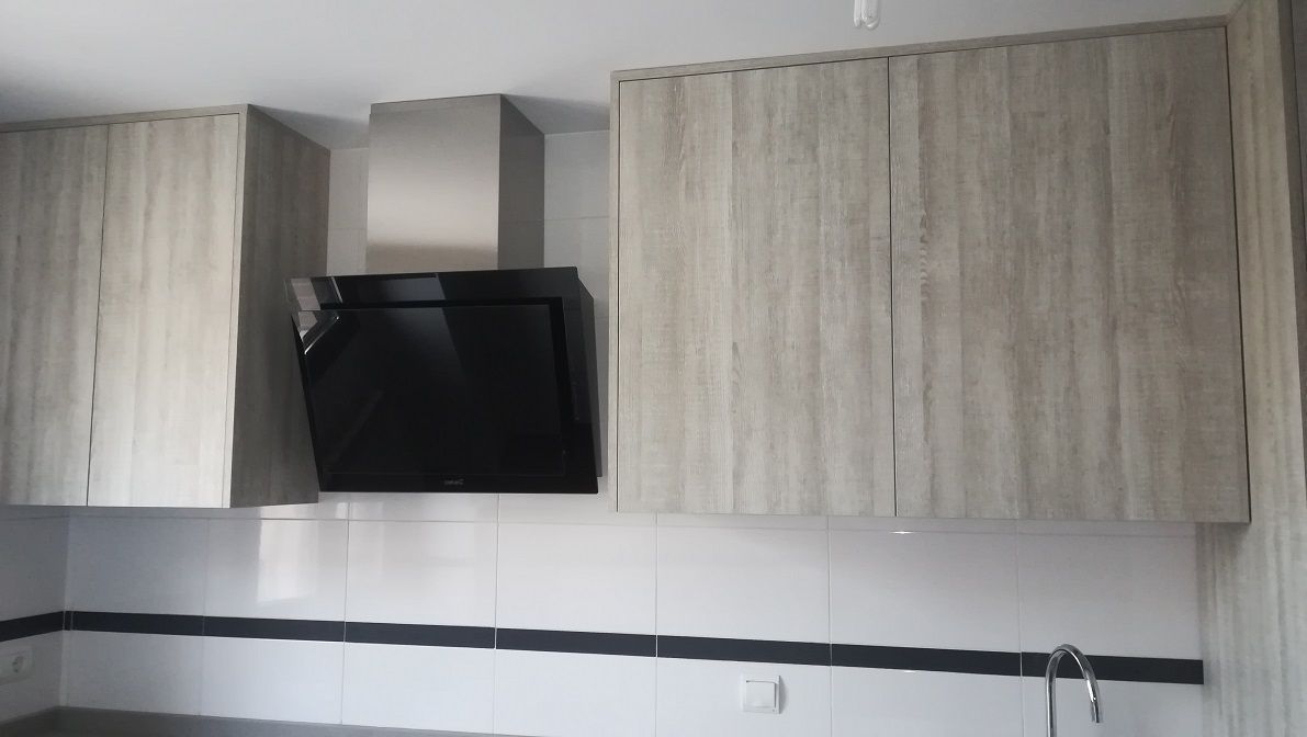 Una zona de cocina con armarios de madera clara, una campana extractora de cristal negro y un salpicadero de azulejos blancos con una franja decorativa negra.