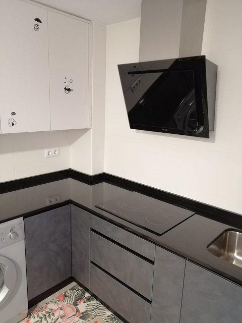 Una cocina moderna con armarios superiores blancos, armarios inferiores gris oscuro, encimera negra y campana extractora angular negra.