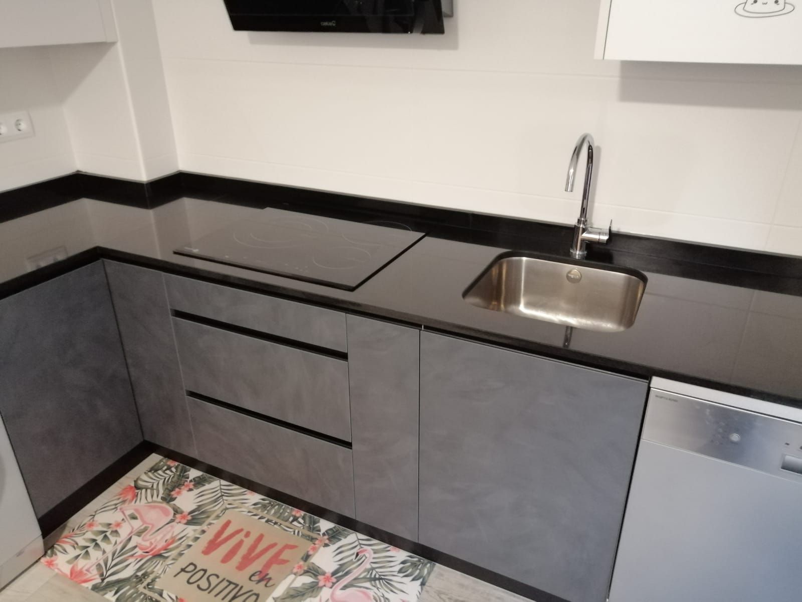 Una cocina moderna con armarios grises, una elegante encimera negra, una placa de inducción y un fregadero de acero inoxidable.