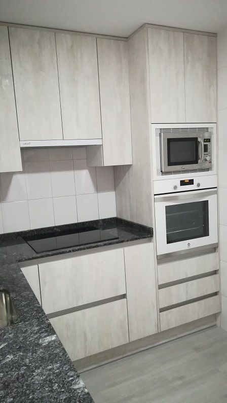Cocina moderna con gabinetes de madera clara, encimeras de granito oscuro y un microondas y horno empotrados.