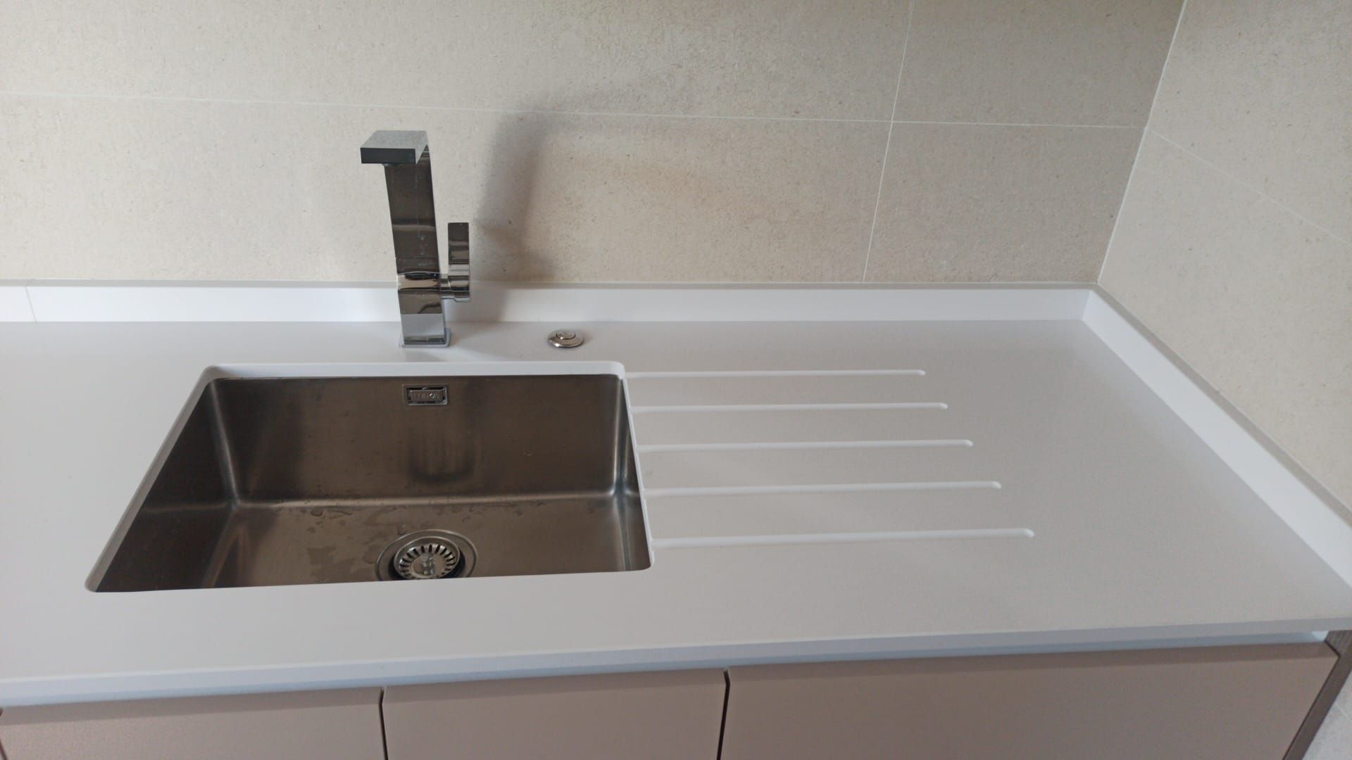 Un moderno fregadero de cocina de acero inoxidable con cubeta rectangular y escurridor, integrado en una encimera blanca y limpia.