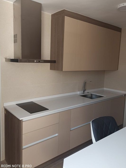 Una cocina moderna con gabinetes color beige, detalles en tonos madera, una placa de cocción integrada, un fregadero de acero inoxidable y una campana extractora.