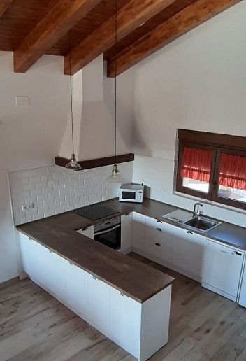 Una cocina blanca en forma de U con encimeras de madera oscura, vigas de techo a la vista y salpicadero de azulejos blancos.