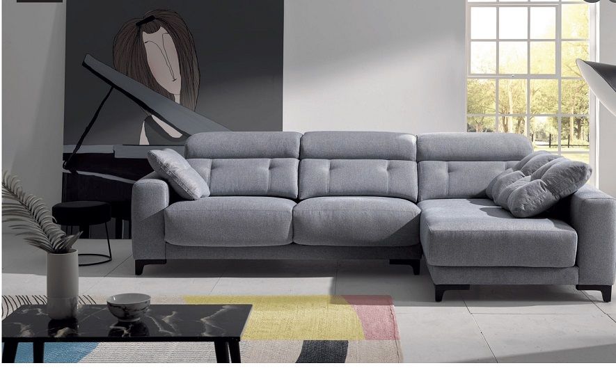 Un sofá modular gris claro con chaise longue, situado en un salón moderno con una alfombra multicolor.