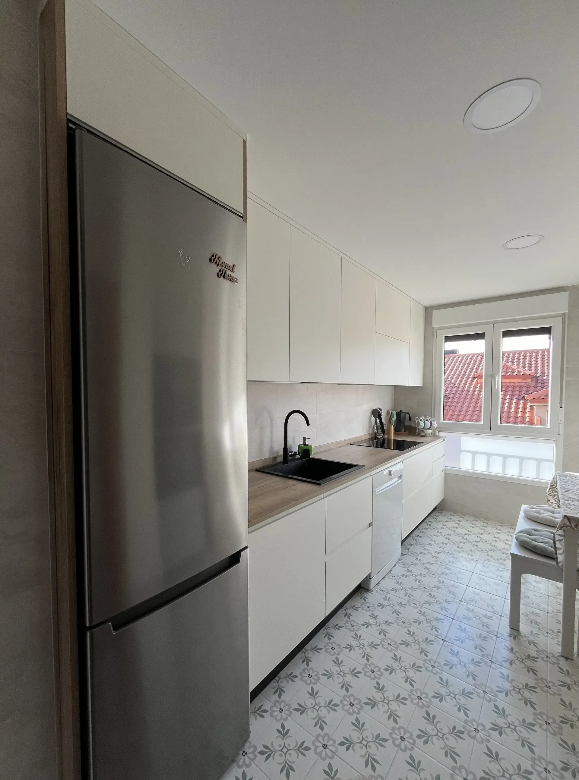 Una cocina moderna con refrigerador de acero inoxidable, gabinetes blancos, fregadero negro y baldosas estampadas en el suelo.