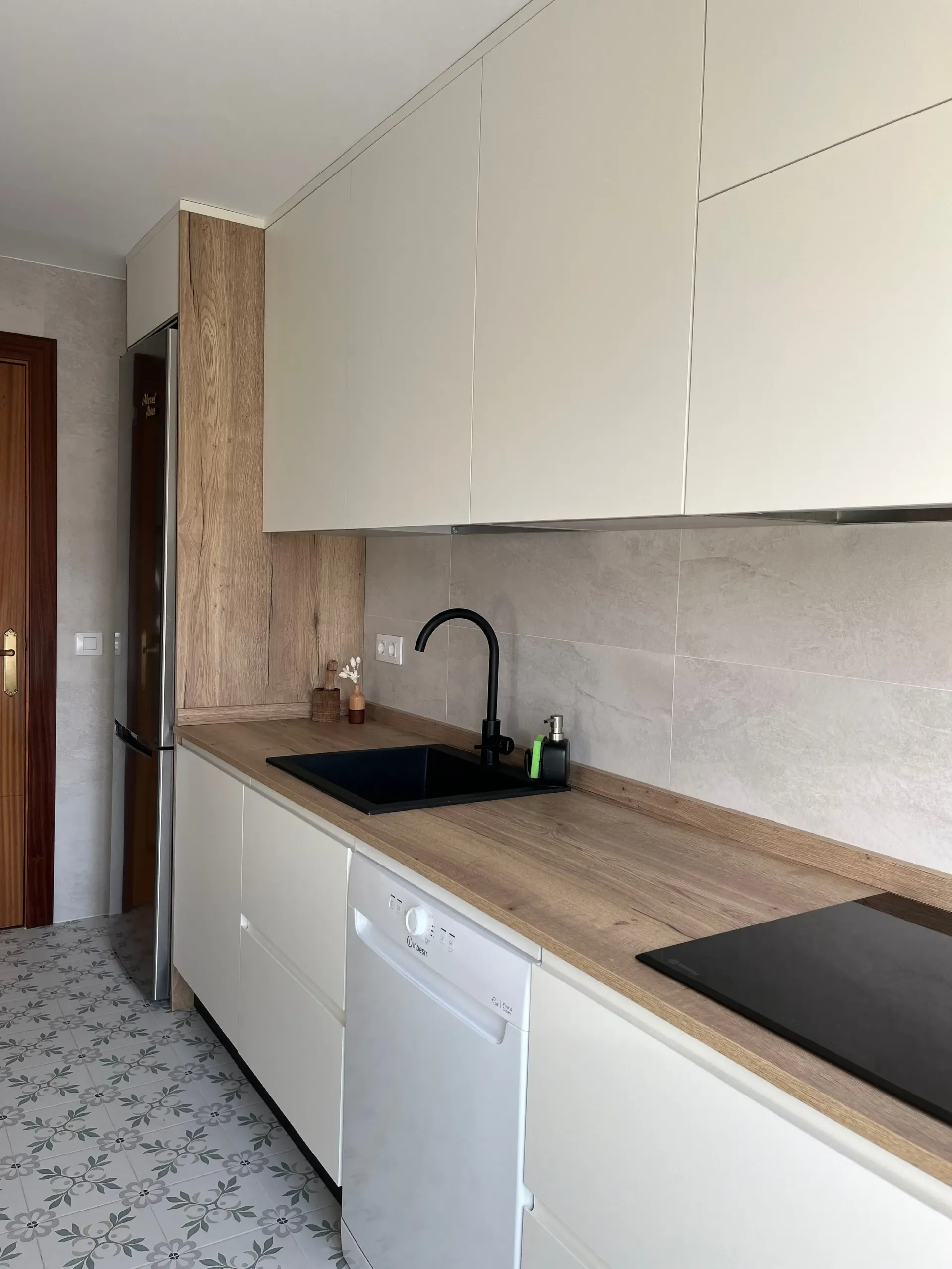 Una cocina moderna con armarios color crema, encimera con acabado de madera, fregadero negro y baldosas estampadas en el suelo.