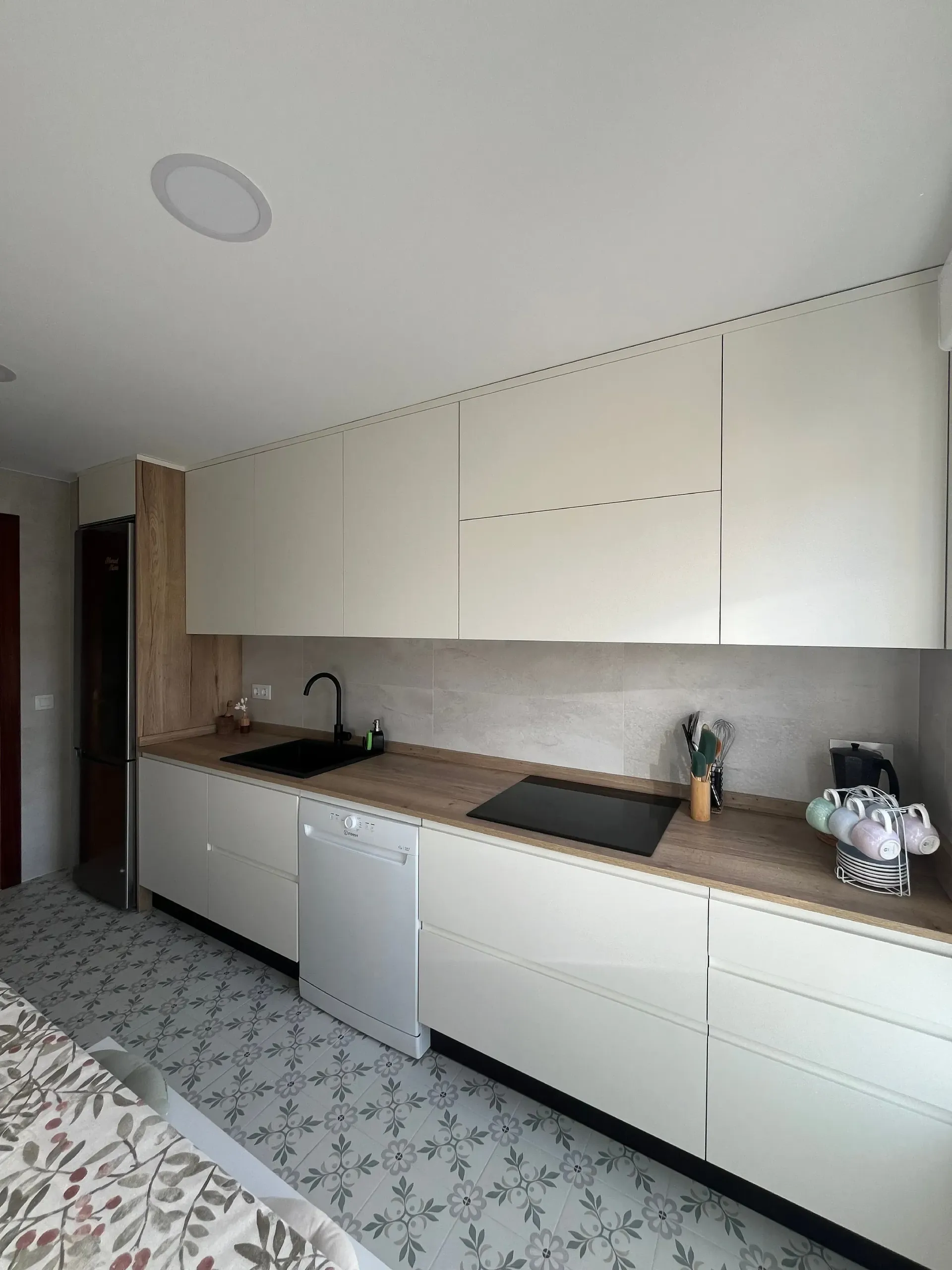 Cocina moderna con armarios blancos, encimera de madera clara, fregadero negro y suelo de baldosas estampadas.