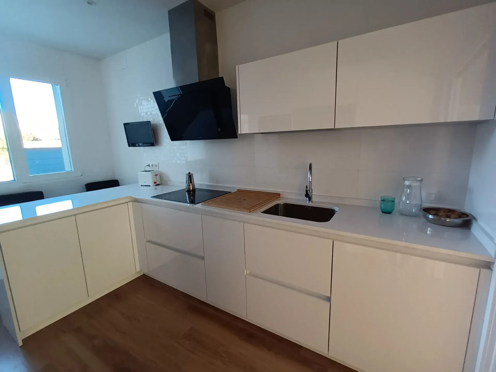 Una cocina moderna con armarios color crema, encimeras blancas, campana extractora negra y suelo con aspecto de madera.