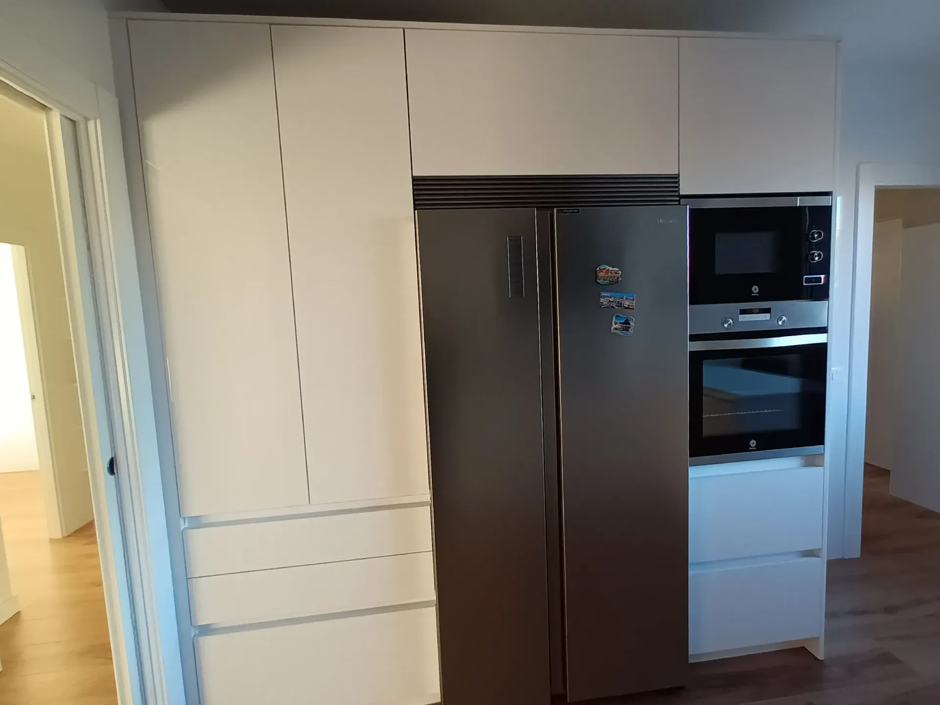Armarios de cocina blancos que van desde el suelo hasta el techo, rodeando un frigorífico de acero inoxidable oscuro y un horno empotrado en la pared.