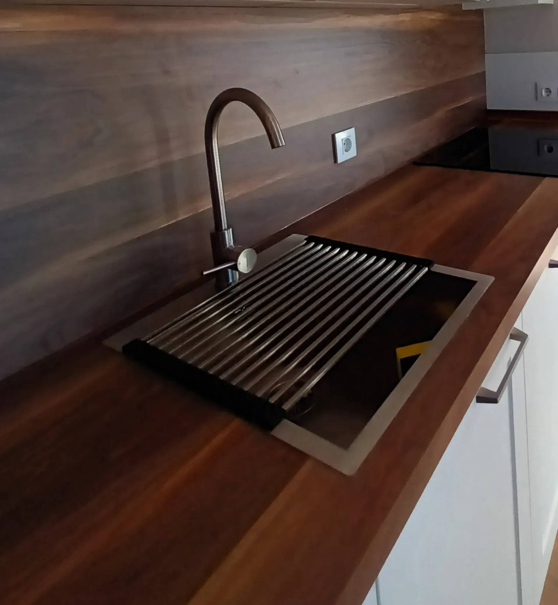 Un fregadero de cocina con un escurridor de metal integrado en una encimera con acabado de madera, que incluye un grifo de bronce curvado.