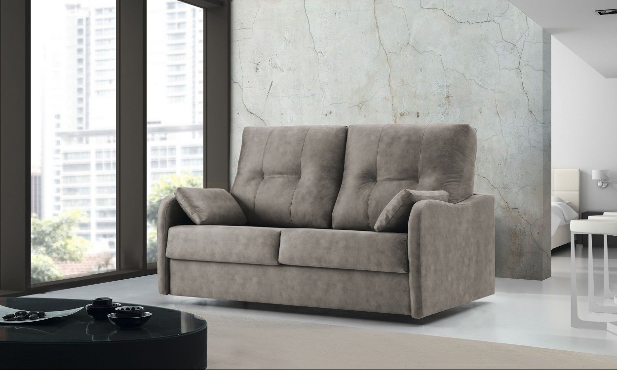 Un sofá beige de dos plazas con cojines capitoné, situado en un salón luminoso y moderno junto a una gran ventana.