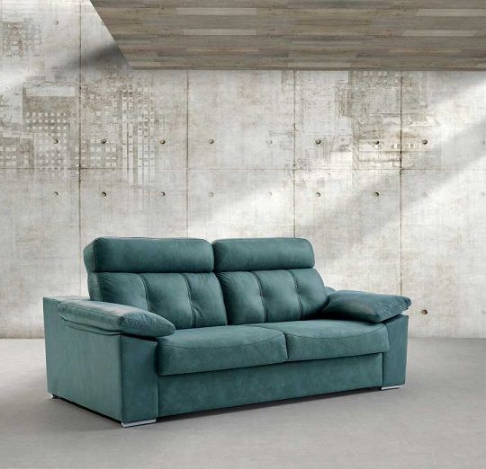 Un sofá tapizado de color verde azulado con dos cojines, centrado contra una pared de hormigón texturizado de color gris claro.