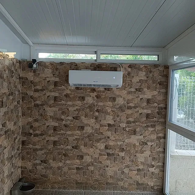Una habitación con una pared de ladrillo y un aire acondicionado blanco colgando del techo.