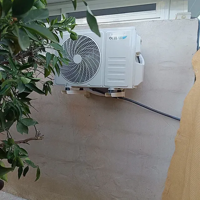 Un acondicionador de aire blanco está colgado en una pared al lado de un árbol.