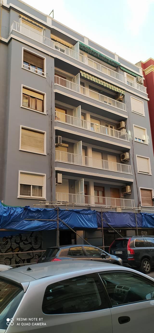 Un edificio con muchas ventanas y coches aparcados delante de él.