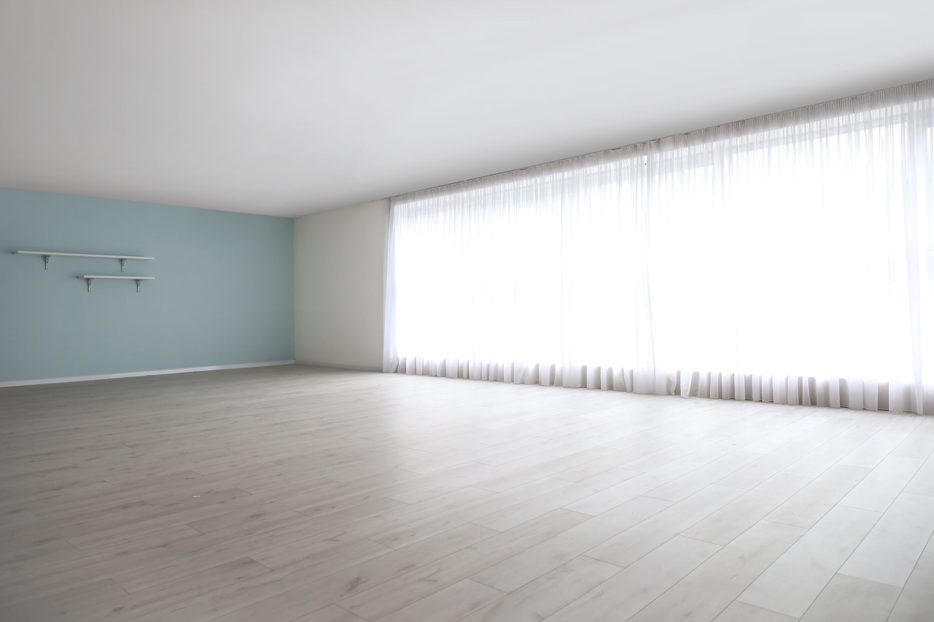 Una habitación vacía con una gran ventana y cortinas blancas.
