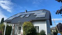 Haus mit dunklem Dach, das renoviert wird, mit Leitern und Gerüsten vor blauem Himmel
