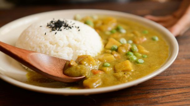 Un plato de curry con arroz y una cuchara de madera sobre una mesa de madera.
