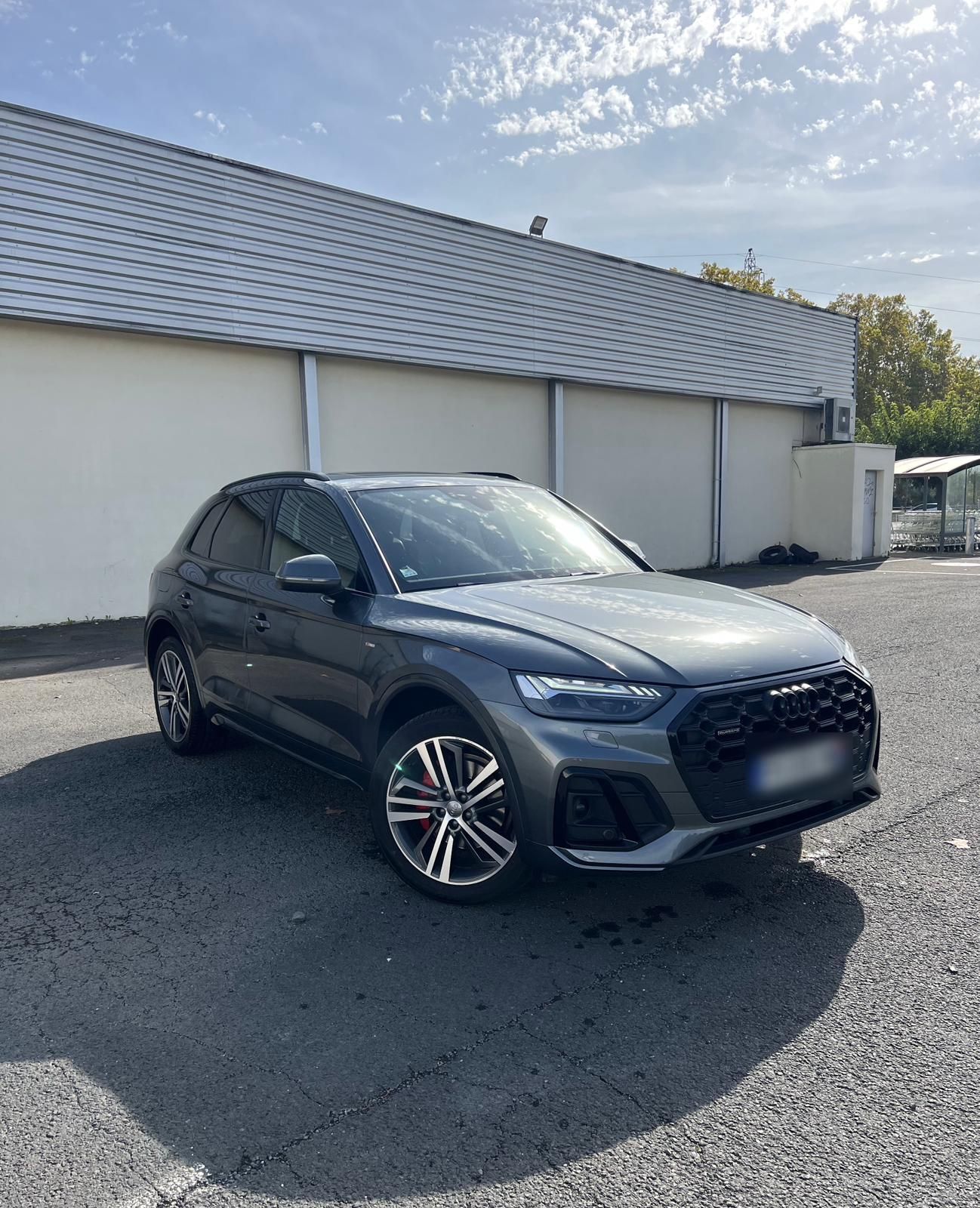 Audi Q5 gris foncé garée devant un bâtiment gris clair par une journée ensoleillée