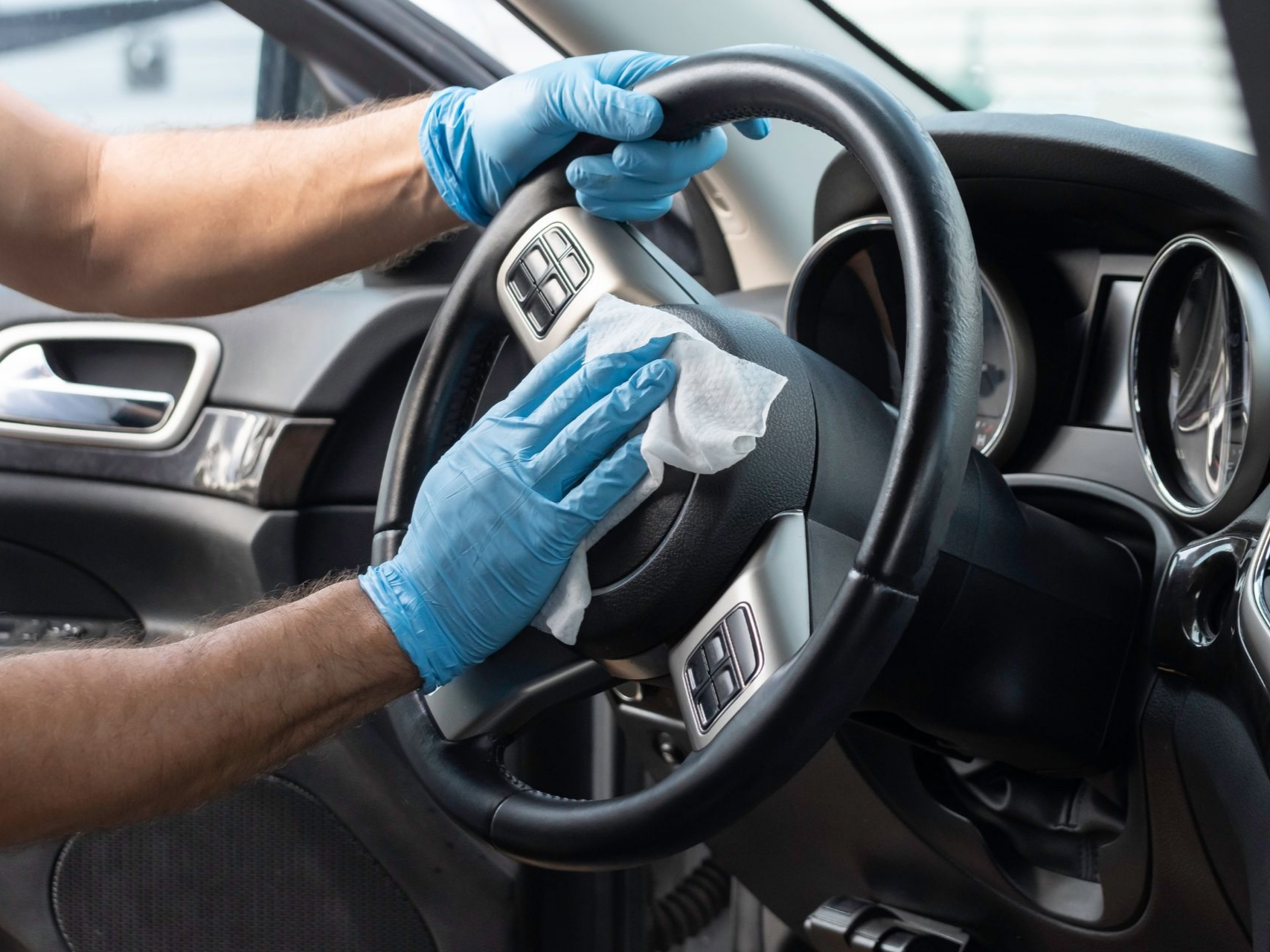 Une personne portant des gants nettoie le volant d'une voiture avec une lingette