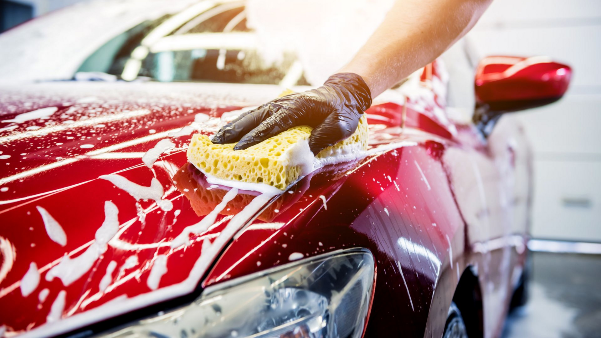 Un homme lave une voiture rouge avec une éponge et du produit moussant
