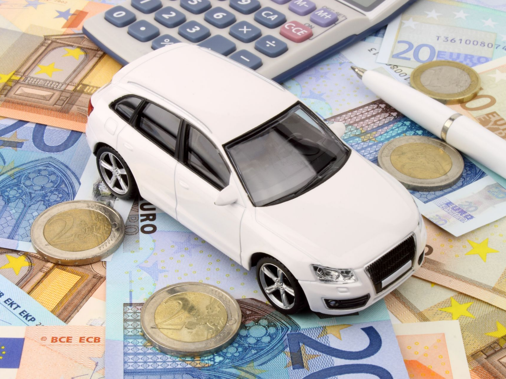 Voiture miniature posée sur des billets avec des pièces, un stylo et une calculatrice