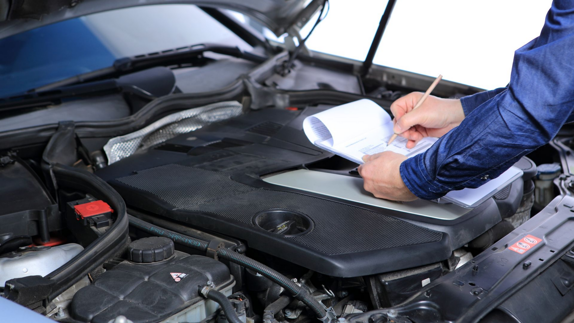 Un homme inspecte sous le capot d'une voiture avec une liste
