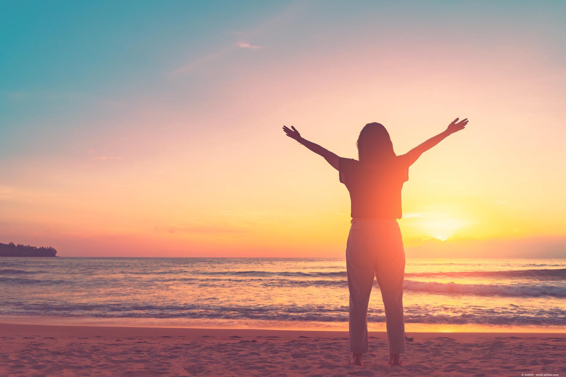 Frau am Meer bei Sonnenaufgang als Symbol für Lebensfreude und Gesundheit