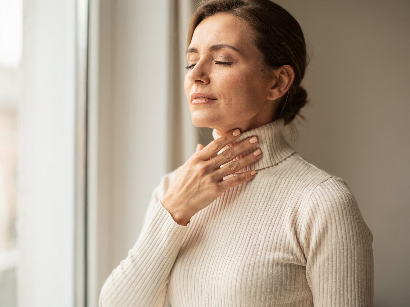 Woman touching her neck with her fingertips in the area of the thyroid