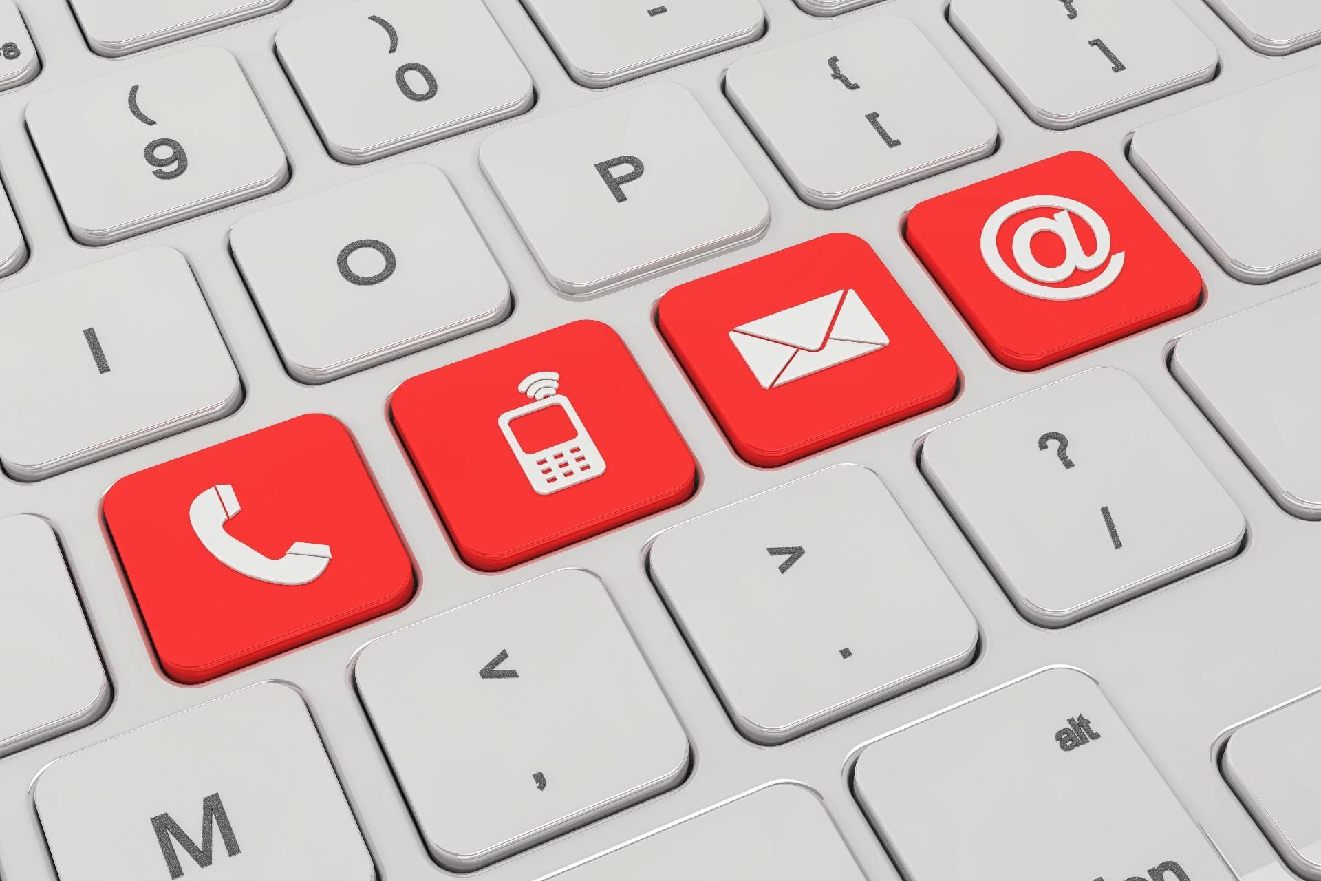 Vier rote Tasten auf einer weißen Computertastatur mit Symbolen für Telefon, Mobilgerät, Briefumschlag und @-Zeichen.