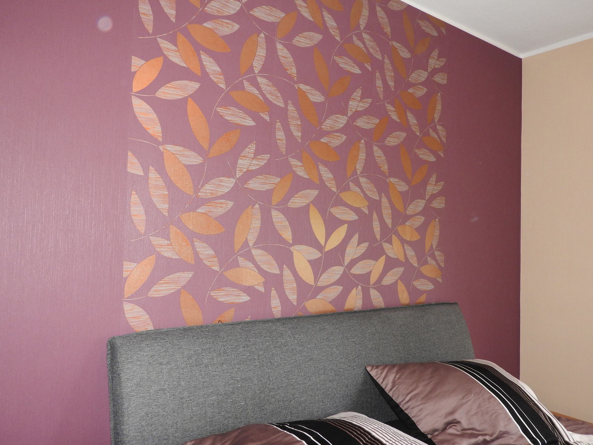 Bordeauxrote Wand mit gold-orangefarbenem Blättermuster hinter dem Kopfteil – ein edler Akzent im Schlafzimmer.