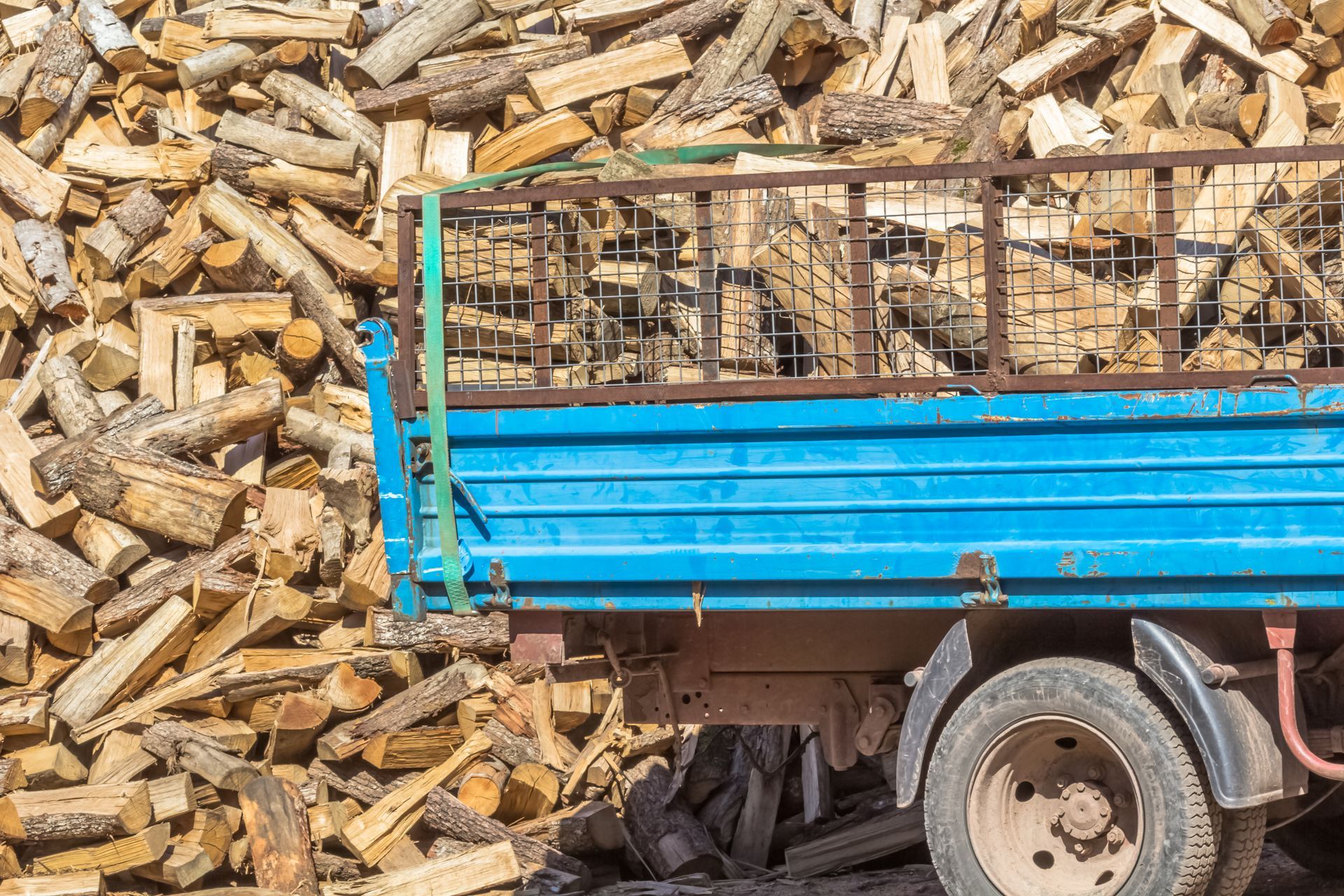 La benne d'un camion bleu rempli de bois de chauffage se trouve à côté d'un gros tas de bois de chauffage.