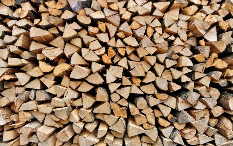 Pile de bois de chauffage empilée, de différentes essences claires et foncées.