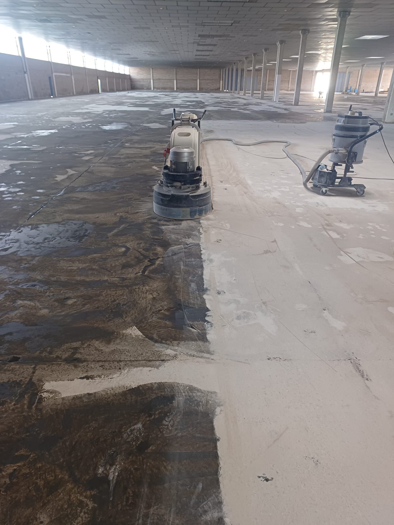 Máquina pulidora de suelos puliendo un suelo de hormigón, una mitad oscura y la otra clara.