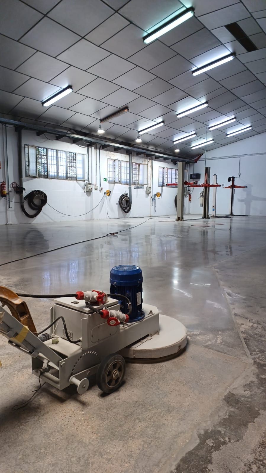 Máquina pulidora de suelos que alisa un suelo de hormigón en un gran almacén de paredes blancas.