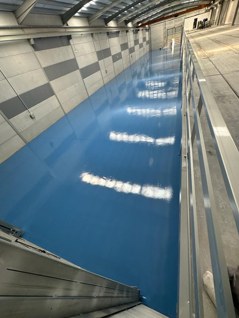 Piscina cubierta rectangular larga con suelo azul, paredes plateadas y techo alto.