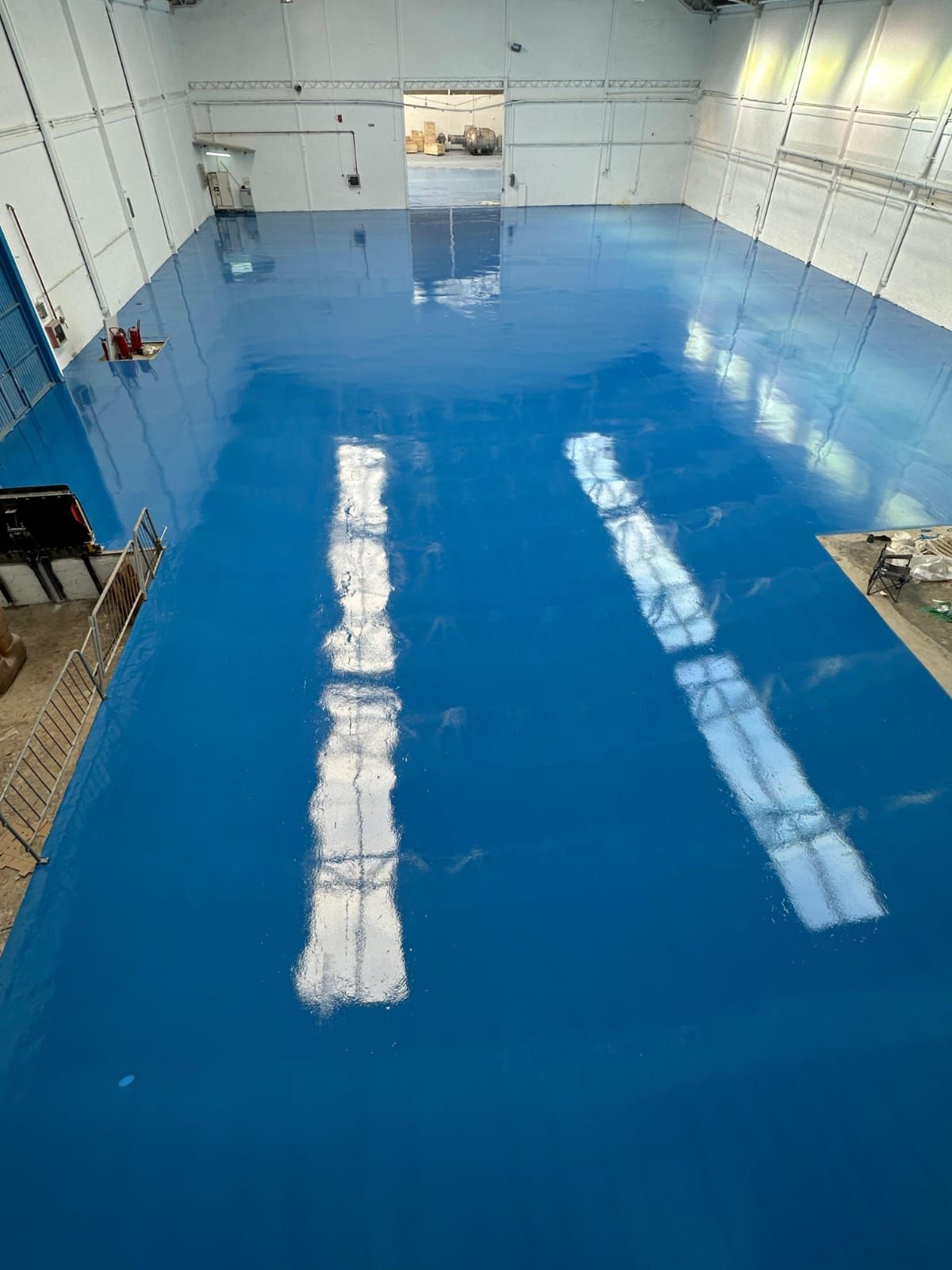 Suelo de epoxi azul en un amplio espacio industrial vacío. Reflejos de luz en la superficie lisa.