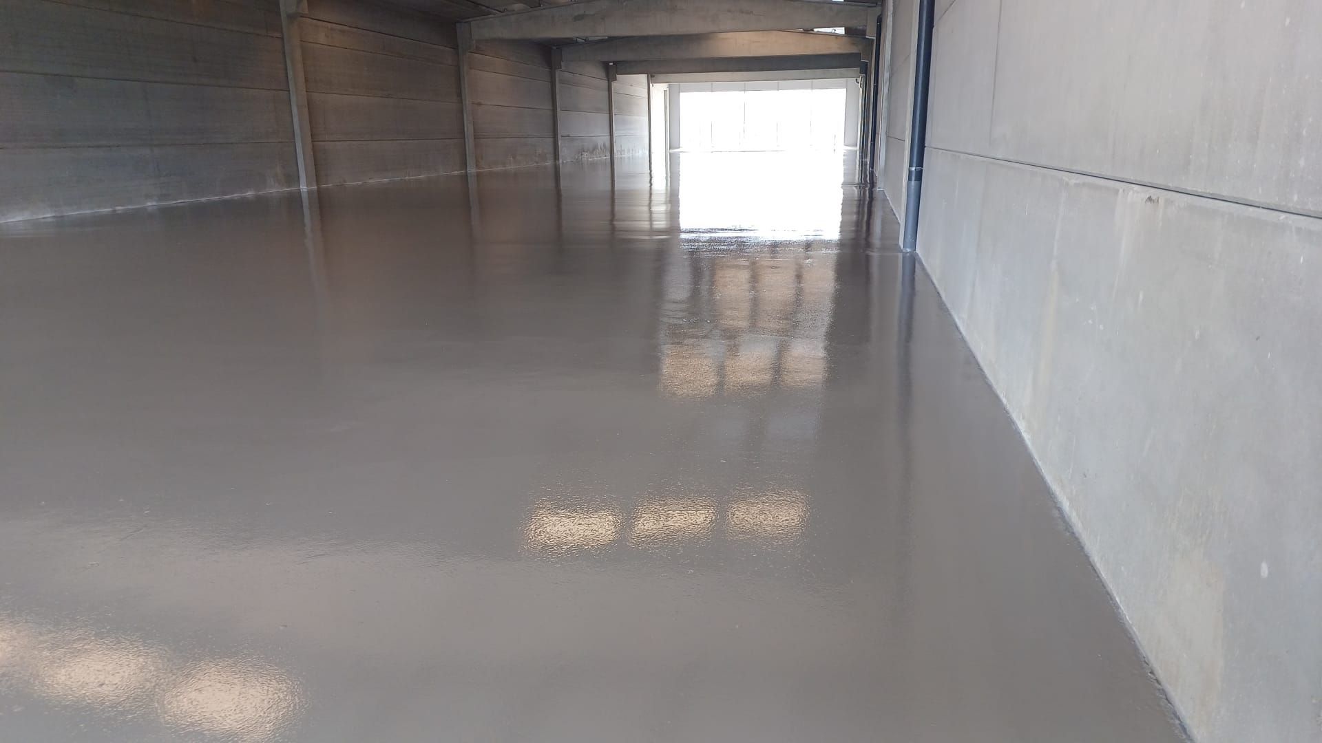 Vista interior de un piso de concreto con un acabado reflectante y brillante, que conduce a una puerta abierta con luz brillante.